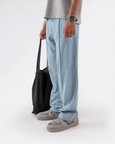 Person wearing light blue trouser and gray shoes holding a black bag on a white background