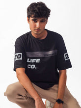 male model wearing black essentials club oversized graphic t shirt showing the front of the shirt while sitting
