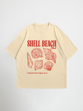 Beige shell beach club oversized graphic t-shirt with red 'Shell Beach Club' text and shell graphics on a light gray background