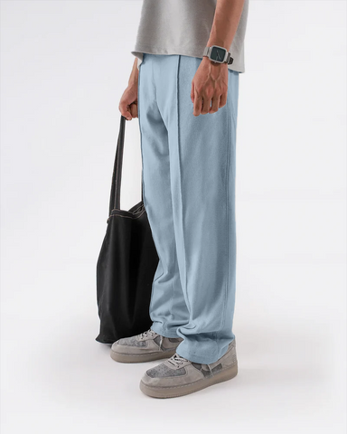 Person wearing light blue trouser and gray shoes holding a black bag on a white background