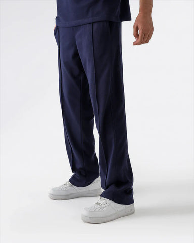 Person wearing navy blue straight pleated trouser and white sneakers on a white background