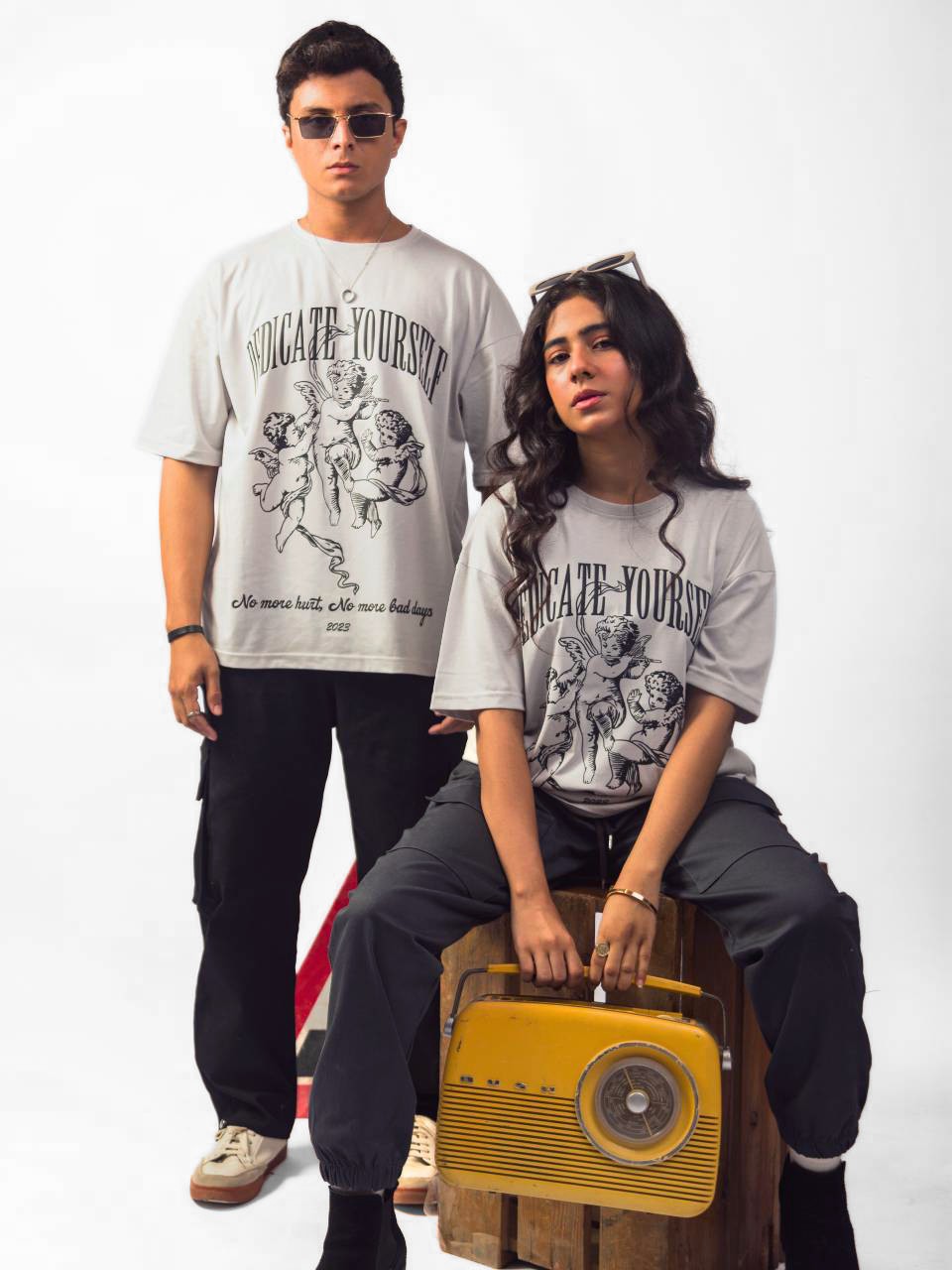 Female and male model wearing grey dedicate yourself oversized graphic t shirt showing front view, male is showing standing position while female showing in sitting position Attire Essentials
