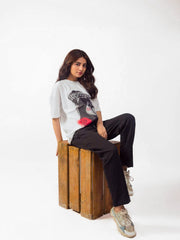 female model wearing white essentials oversized graphic t shirt showing the  side view while sitting on a wooden block