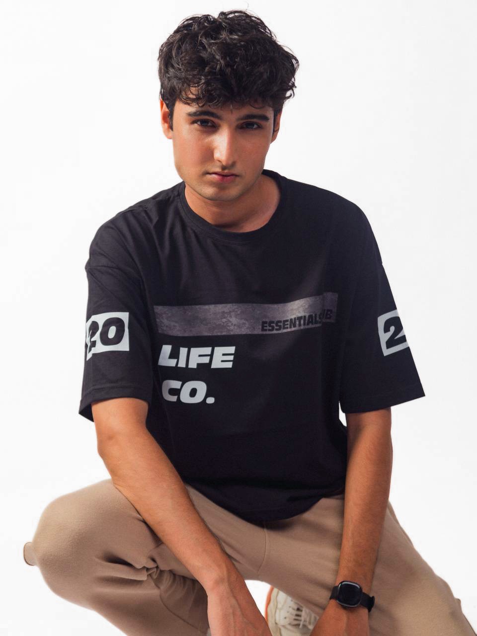 male model wearing black essentials club oversized graphic t shirt showing the front of the shirt while sitting