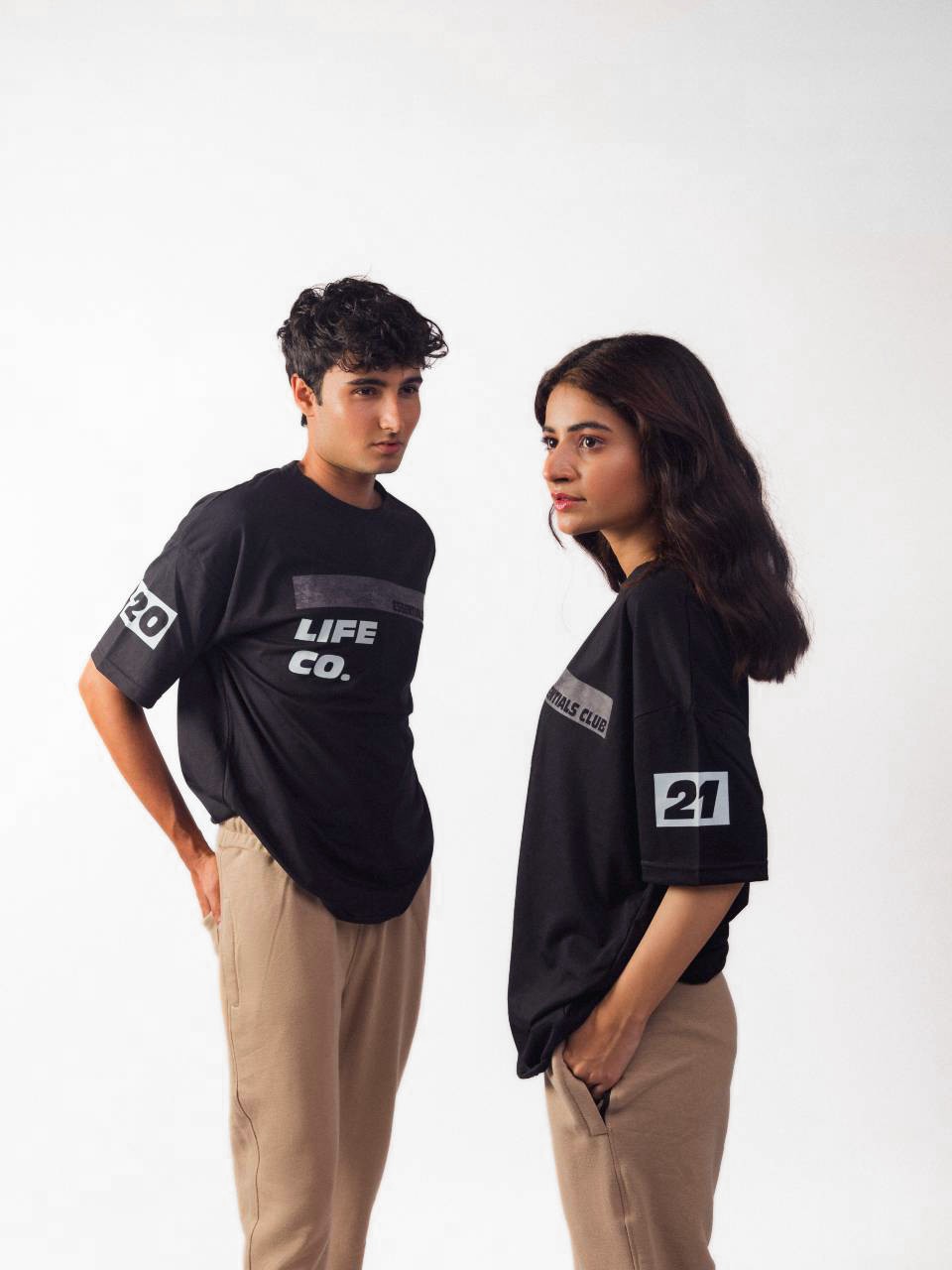 male and femal model wearing black essentials club oversized graphic t shirt showing the side view of the t shirt