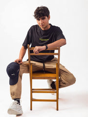Male model wearing black kanye west oversized graphic t shirt showing the front side of the t shirt in sitting position Attire Essentials