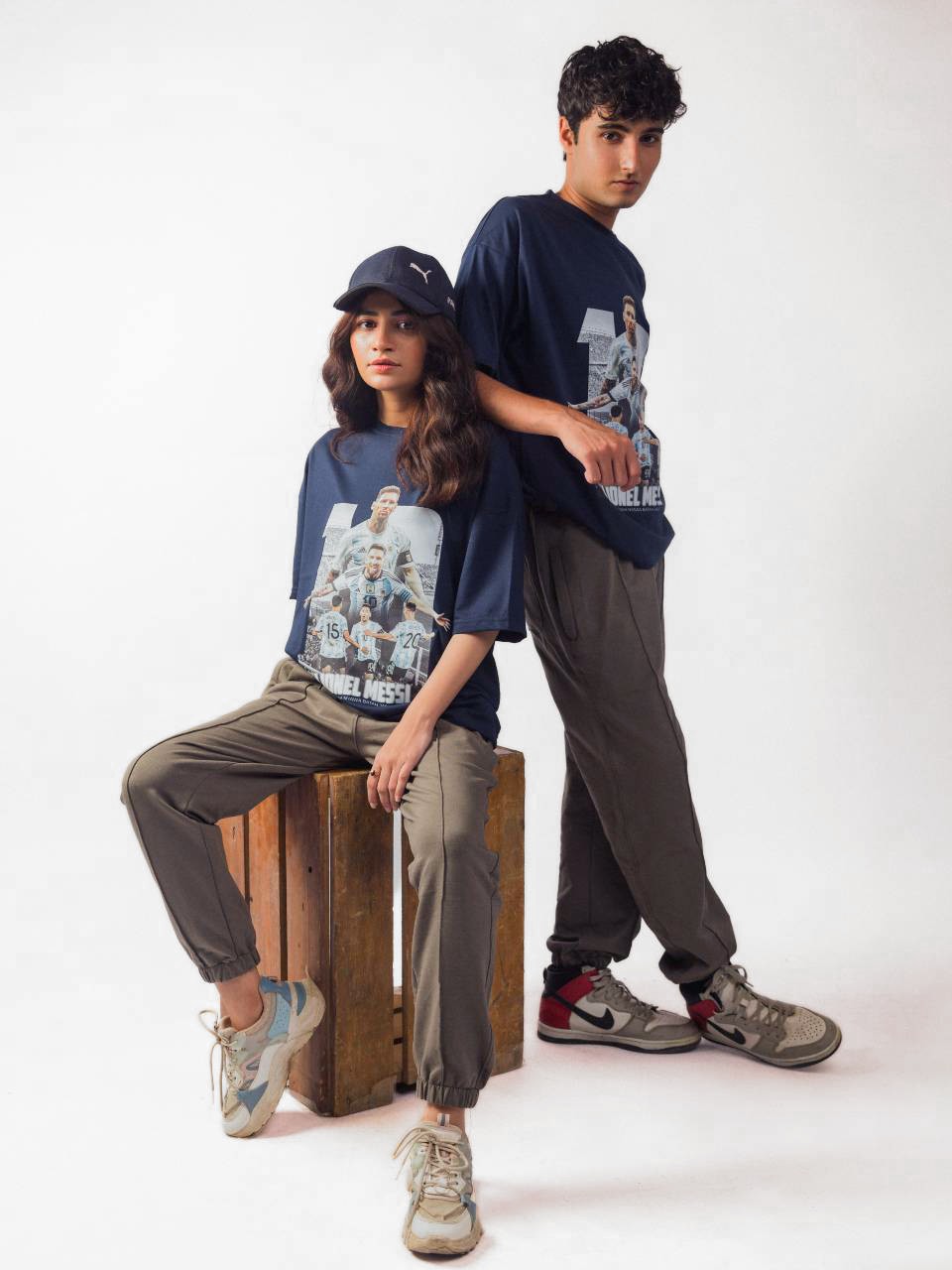 male and female model showing blue lionel messi oversized graphic t shirt, male model showing the side view while female showing the front view in sitting position