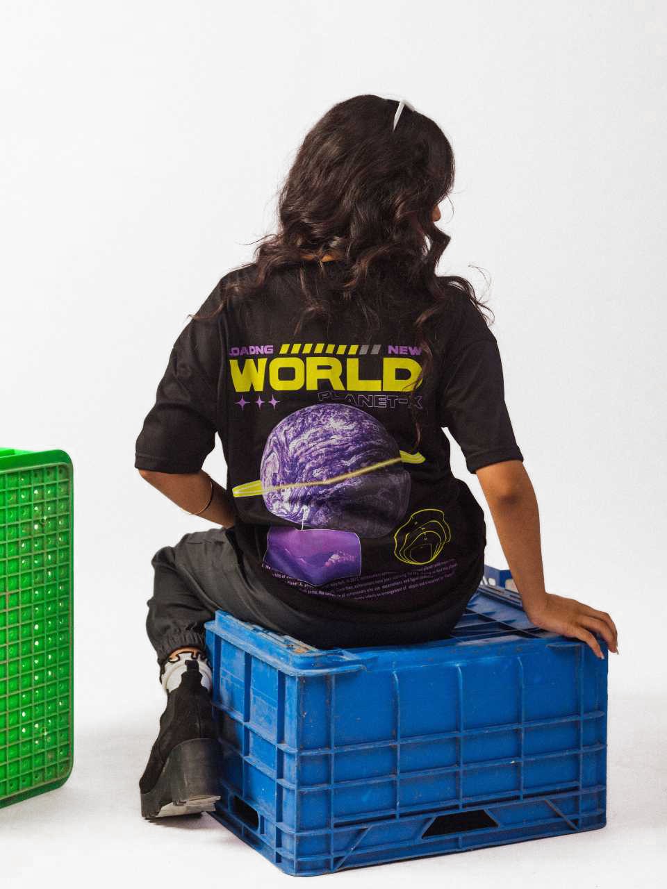 female model wearing black loading new world oversized graphic t shirt in which female model showing the back side of the t shirt in sitting position