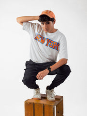 male model wearing white newyork oversized graphic t shirt showing front side while sitting on a wooden box